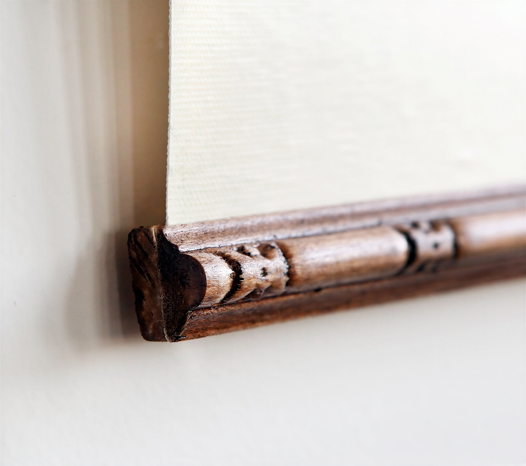 a close-up view of a wooden frame with intricate carvings, mounted on a white wall.